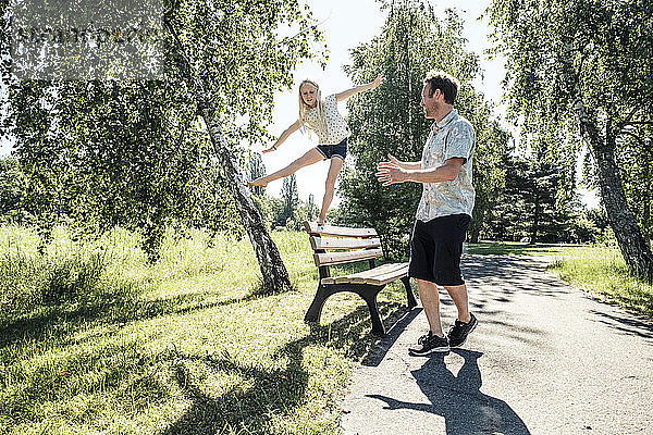 Vater beobachtet Tochter beim Balancieren auf einer Parkbank