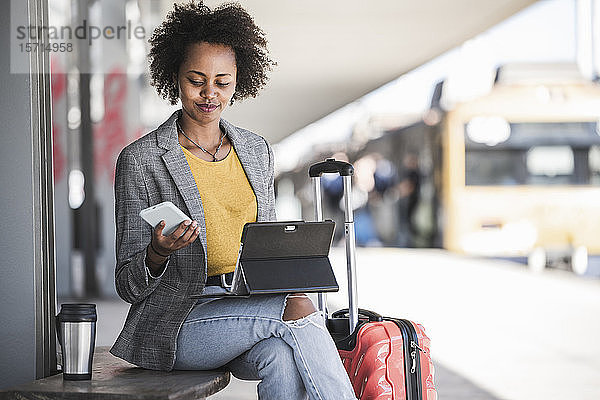 Junge Geschäftsfrau mit Tablet und Smartphone am Bahnhof