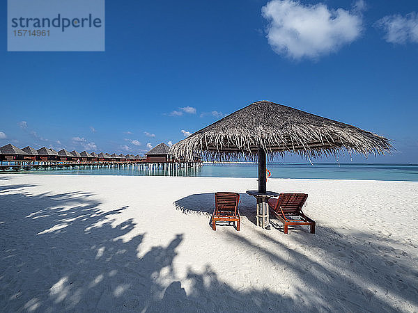 Malediven  Leere Liegestühle unter Strohschirm am sandigen Küstenstrand im Sommer