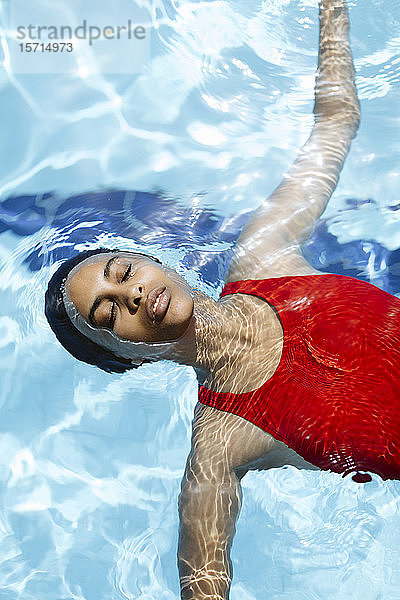 Porträt einer jungen Frau mit geschlossenen Augen  die auf Wasser im Schwimmbad schwimmt