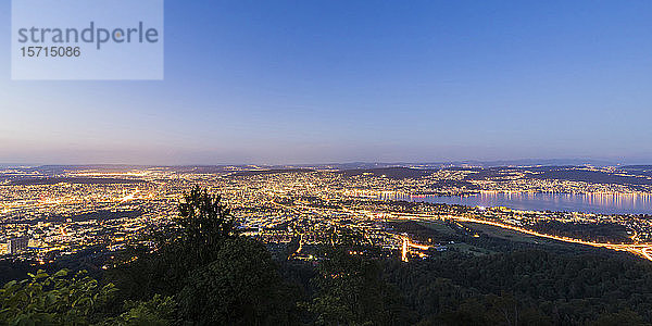 Schweiz  Kanton Zürich  Zürich  Panoramaansicht der beleuchteten Stadt vom Gipfel des Uetlibergs in der Abenddämmerung gesehen