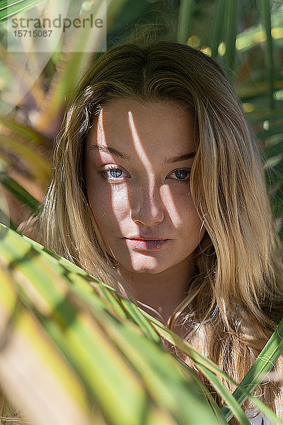 Porträt einer blonden jungen Frau zwischen Palmenblättern