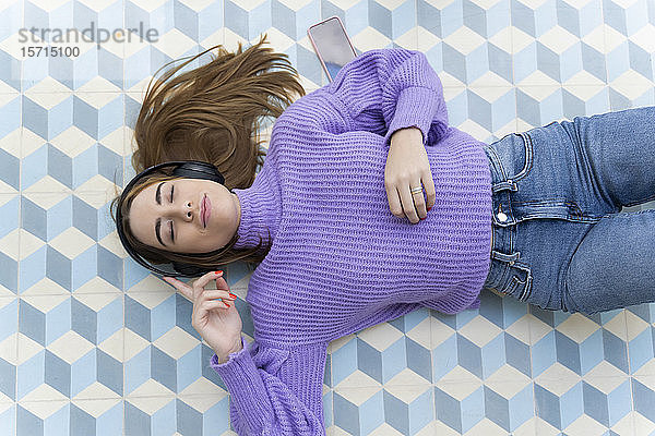Porträt einer auf dem Boden liegenden jungen Frau mit geschlossenen Augen  die mit Kopfhörern Musik hört
