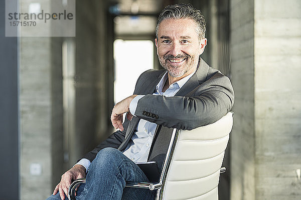 Porträt eines lächelnden reifen Geschäftsmannes  der auf einem Stuhl im Büro sitzt