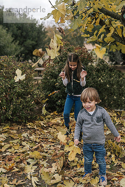 Kleine Jungen und Mädchen spielen im Herbst mit Blättern