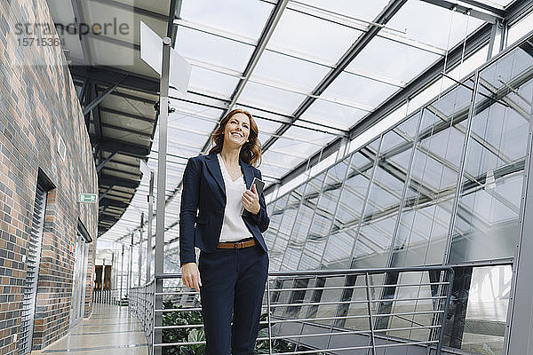 Lächelnde Geschäftsfrau mit einer Tablette in der Hand in einem modernen Bürogebäude