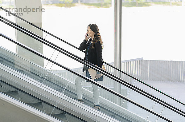 Lächelnde Geschäftsfrau auf der Rolltreppe beim Telefonieren
