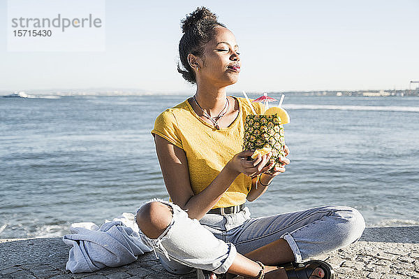 Junge Frau sitzt am Wasser und genießt ein Getränk in einer Ananas  Lissabon  Portugal