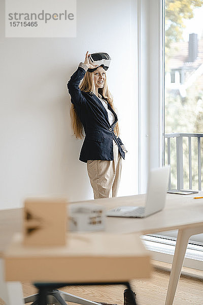 Lächelnde junge Geschäftsfrau mit VR-Brille im Büro