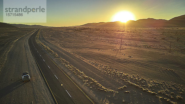 Jeep auf schmutziger Piste in der Namib-Wüste mit der Sonne hinter den Dünen versteckt  Namibia