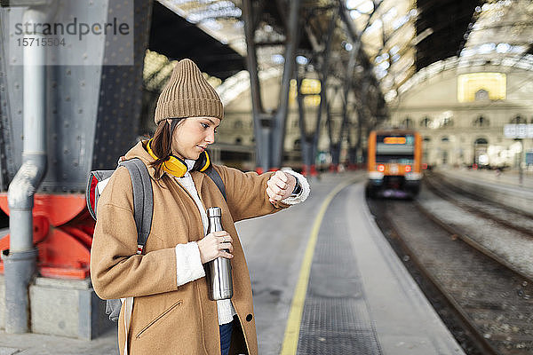 Junge Frau prüft die Uhrzeit am Bahnhof