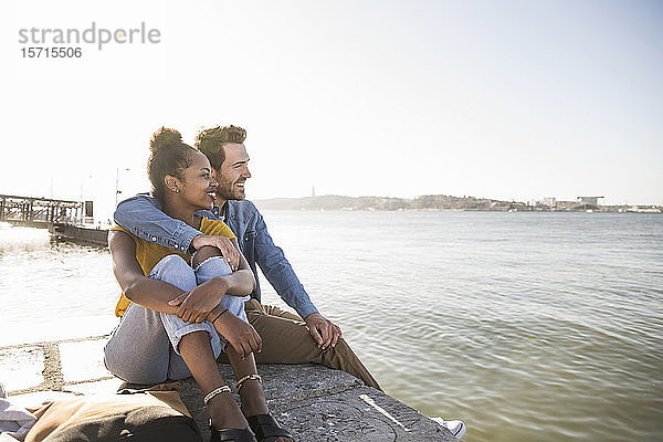 Junges Paar sitzt am Pier am Wasser und genießt die Aussicht  Lissabon  Portugal