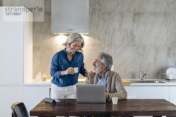 Glückliches reifes Paar mit Laptop auf dem Küchentisch zu Hause