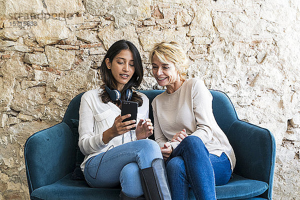 Porträt von zwei Kollegen  die auf der Couch sitzen und auf ein Smartphone schauen