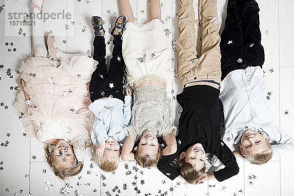 Gruppenbild von fünf Kindern  die kopfüber auf dem Boden liegen und von Weihnachtskonfetti bedeckt sind