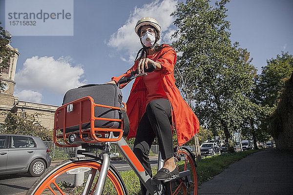 Junge Frau mit Helm und Gesichtsmaske  Fahrradfahren in der Stadt