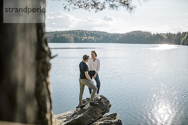 Glückliches Paar auf einem Felsen am Seeufer stehend  Forstsee  Kärnten  Österreich