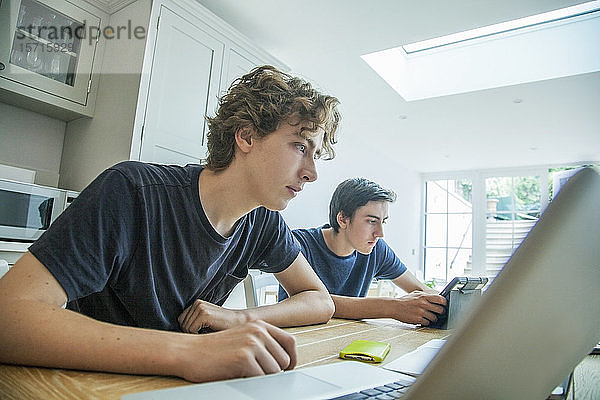 Zwei Jungen im Teenager-Alter benutzen zu Hause Laptop und Tablett auf dem Tisch