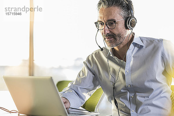 Älterer Geschäftsmann trägt Kopfhörer mit Laptop am Schreibtisch im Büro