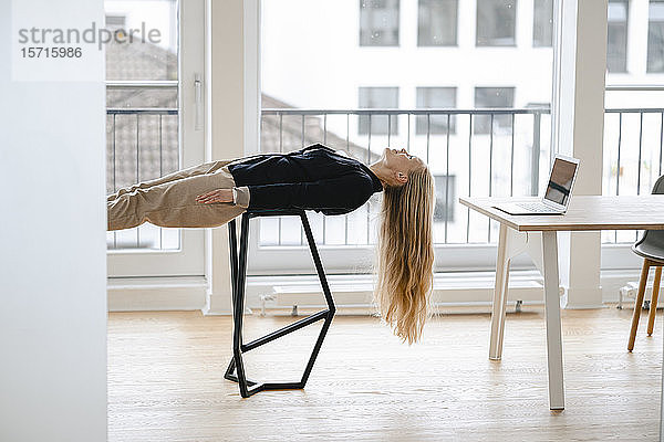 Junge Geschäftsfrau  die im Büro auf einem Hocker liegend Yoga praktiziert
