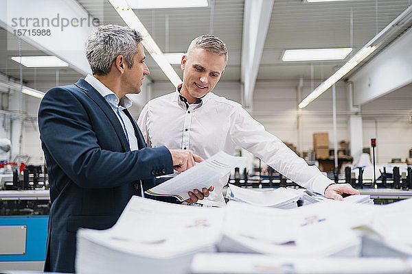 Zwei Geschäftsleute diskutieren in einer Fabrik über Papier