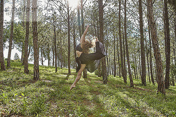 Barfüßige junge Frau springt im Wald in die Luft