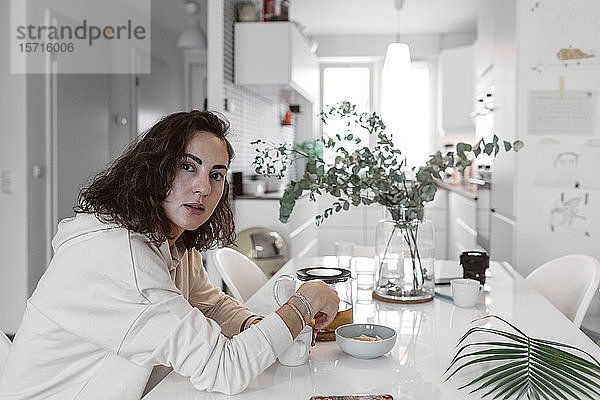 Porträt einer Frau  die am Küchentisch sitzt und Tee trinkt