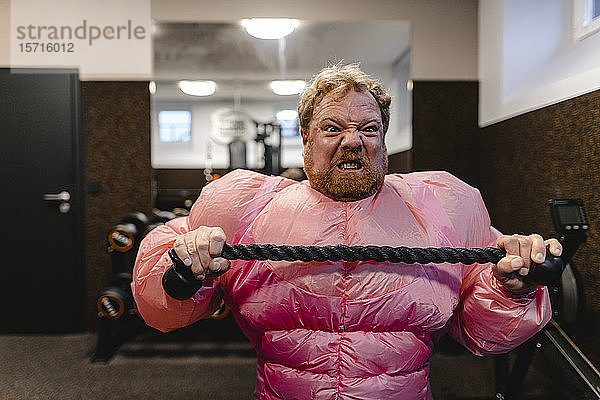 Mann in rosa Bodybuilder-Kostüm übt im Fitnessstudio