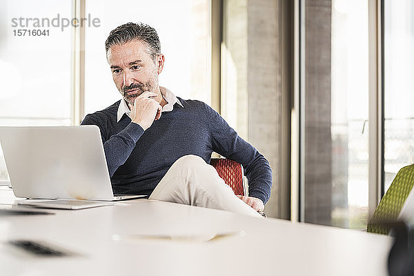 Reifer Geschäftsmann sitzt am Schreibtisch im Büro und benutzt einen Laptop
