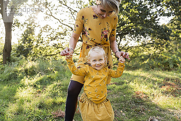 Porträt eines kleinen blonden Mädchens Hand in Hand mit ihrer Mutter auf einer Wiese