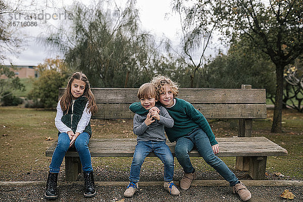 Gruppenbild von drei Kindern  die auf einer Holzbank im Freien sitzen