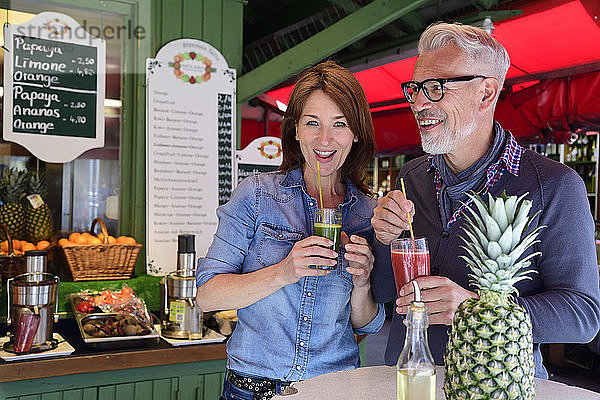 Porträt eines glücklichen reifen Paares  das an einem Marktstand einen gesunden Saft trinkt