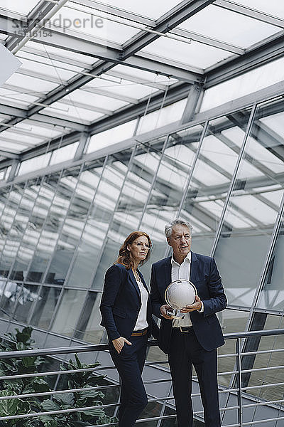 Geschäftsmann und Geschäftsfrau halten Globus in modernem Bürogebäude