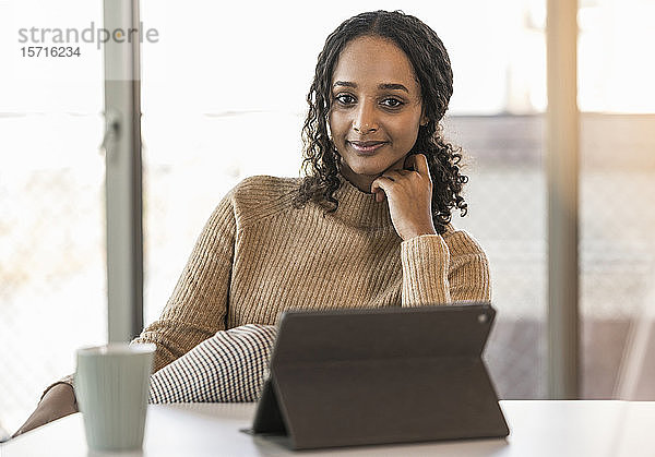 Porträt einer lächelnden jungen Geschäftsfrau  die mit einem Tablett am Schreibtisch im Büro sitzt