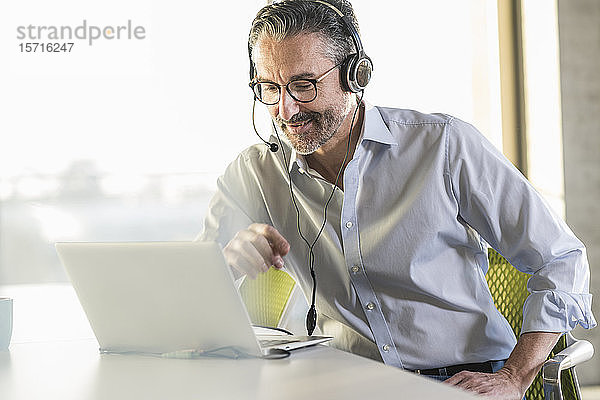 Älterer Geschäftsmann trägt Kopfhörer mit Laptop am Schreibtisch im Büro