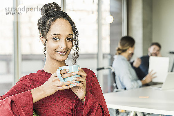 Porträt einer lächelnden jungen Geschäftsfrau bei einer Kaffeepause während einer Besprechung im Büro