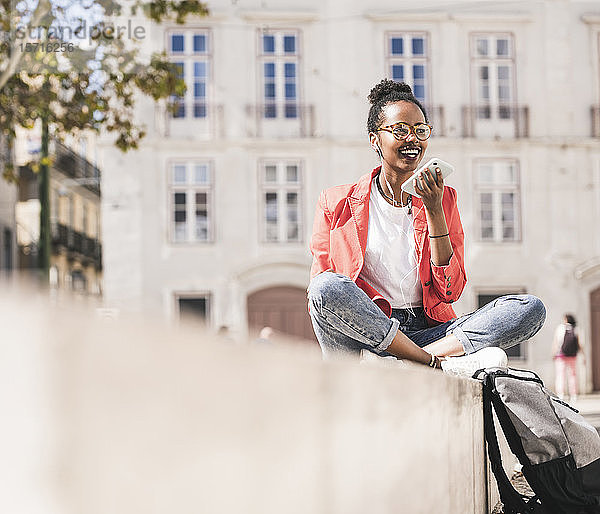 Lächelnde junge Frau mit Kopfhörern und Smartphone in der Stadt  Lissabon  Portugal