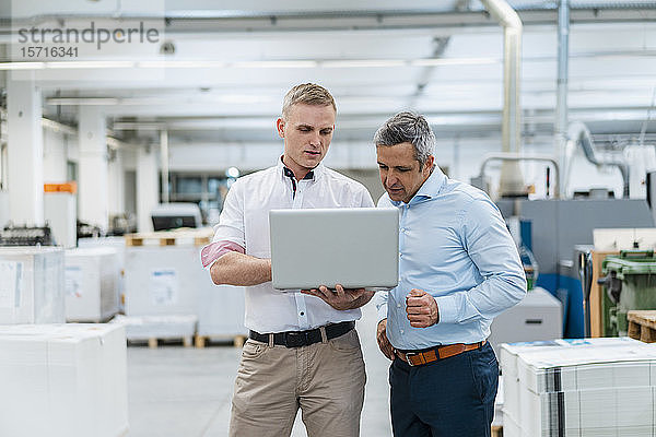 Zwei Kollegen diskutieren mit Laptop in einer Fabrik