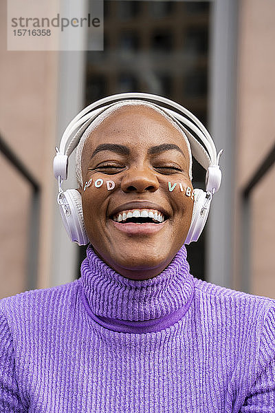 Porträt einer weißhaarigen Frau mit weißen Kopfhörern und Aufklebern im Gesicht  die Musik hört und lacht