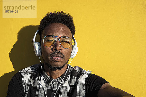 Porträt eines jungen Mannes  der mit Kopfhörern an der gelben Wand Musik hört