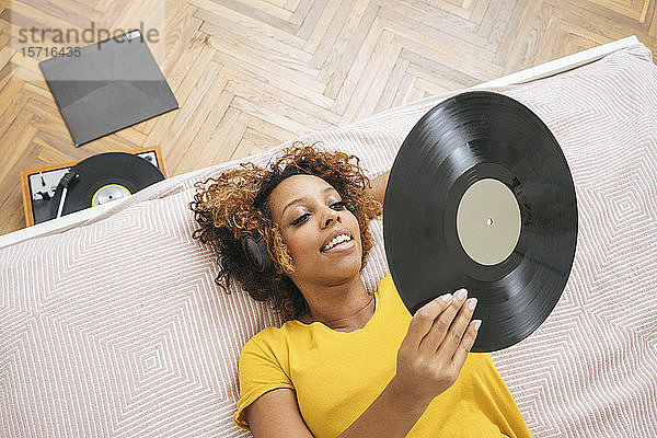 Junge Frau liegt auf dem Bett und hört Musik mit Kopfhörern und Plattenspieler