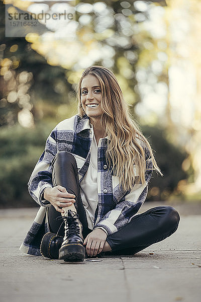 Porträt einer lächelnden jungen Frau  die im Freien auf dem Boden sitzt