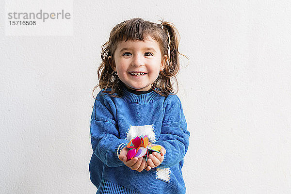 Glückliches kleines Mädchen  das auf einer Party vor einer weißen Wand Konfetti bläst