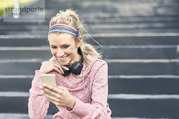 Sportliche Frau sitzt auf einer Treppe und benutzt ein Smartphone