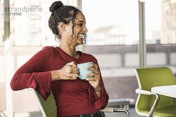 Glückliche junge Geschäftsfrau mit Kaffeepause im Büro
