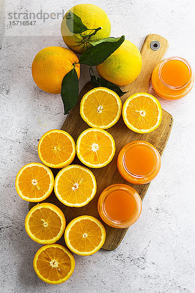 Frisch geschnittene Orangen und Gläser mit Orangensaft auf Schneidebrett