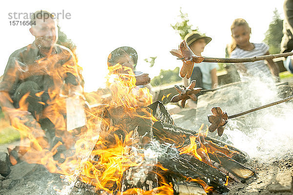 Kinder braten Würstchen am Lagerfeuer an Stöcken