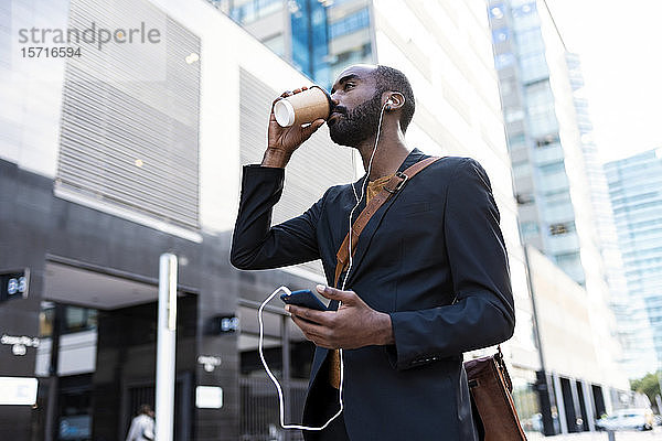 Junger Geschäftsmann mit Kopfhörern und Smartphone  der Kaffee trinkt  um ins Freie zu gehen