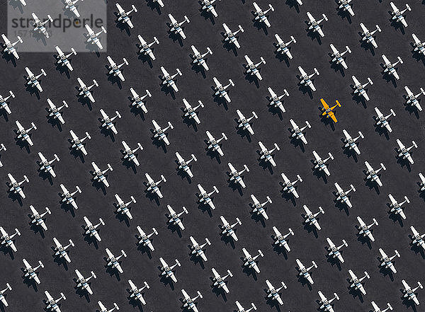Luftbild eines einzelnen orangefarbenen Flugzeugs  umgeben von ausschließlich weißen Flugzeugen