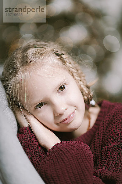 Porträt eines kleinen blonden Mädchens  das zu Hause einen rubinroten Strickpullover trägt